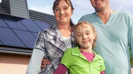Eine kleine Familie, im Hintergrund ist ein Haus mit einer Photovoltaikanlage