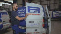 Ein Handwerker öffnet die Tür eines Lieferwagens mit dem Logo von Biefang, um seine Werkzeuge für die Arbeit zu holen.