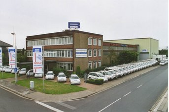 Ein modernes Firmengebäude mit mehreren weißen Fahrzeugen, die ordentlich auf dem Parkplatz aufgereiht sind.
