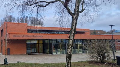 Die moderne Heinrich-Pattberg-Realschule zeigt eine orangefarbene Fassade und große Fenster, umgeben von kahlen Bäumen.