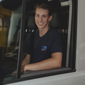 Der Fahrer eines Fahrzeugs lächelt freundlich aus dem Fenster, während er in einem sportlichen T-Shirt posiert.