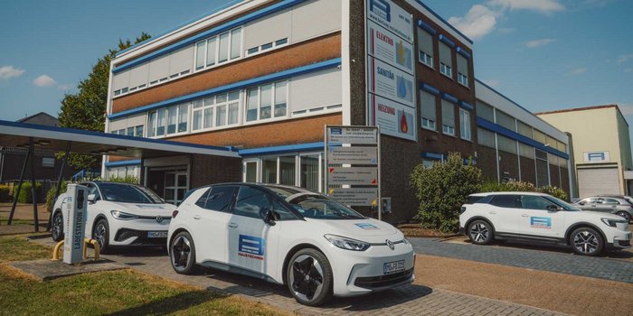 Drei Elektroautos stehen vor einem modernen Gebäude mit blauen Akzenten und einem Schild für Haustechnik-Dienstleistungen.