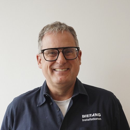 Ein lächelnder Mann mit Brille trägt ein dunkelblaues Hemd mit dem Aufdruck 'BIEFANG Installationen'.