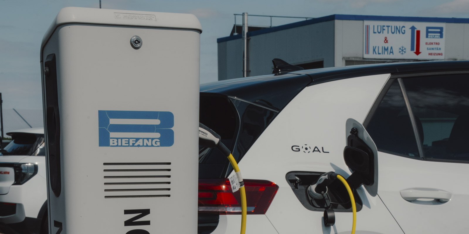 Eine Elektro-Ladestation mit dem Logo 'BIEFANG' steht neben einem weißen Auto, das aufgeladen wird.