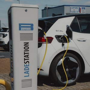 Ein Elektroauto wird an einer Ladestation aufgeladen, während im Hintergrund ein klarer Himmel zu sehen ist.